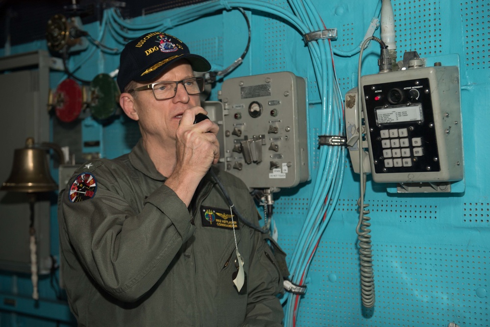 Commander, Carrier Strike Group 3, Rear Adm. Mike Wettlaufer, uses the 1MC system in the pilot house of USS Chung-Hoon (DDG 93) to address the  crew.