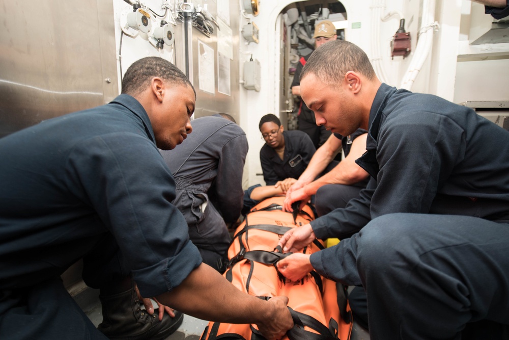 Ship’s Serviceman Seaman Apprentice Logan Parker, left, and Quartermaster Seaman Jordan Hall strap a simulated wounded Sailor into a stretcher during a medical training exercise aboard USS Chung-Hoon (DDG 93).