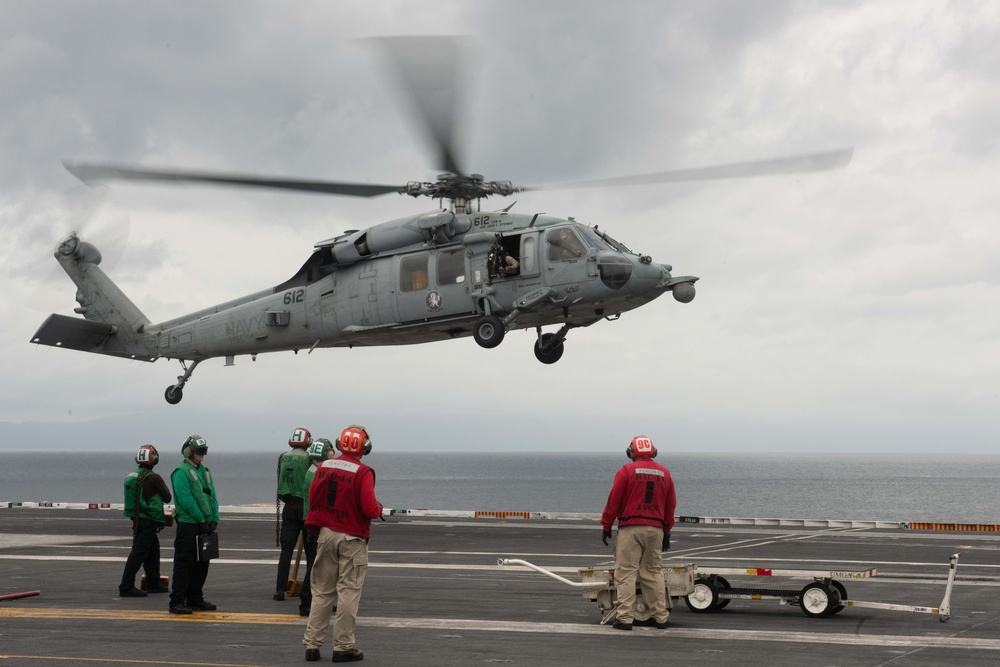 Sailors watch as an MH-60S Knight Hawk, with Helicopter Sea Combat Squadron (HSC) 14, prepares to land on the flight deck aboard USS John C. Stennis (CVN 74).
