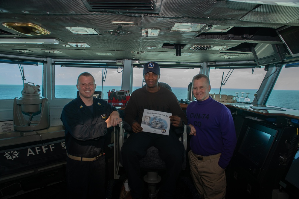 Airman Ernest Odeh poses for a photograph as the Sailor of the Day with Capt. Randy Peck, right, commanding officer of USS John C. Stennis (CVN 74), and Command Master Chief Benjamin Rushing.