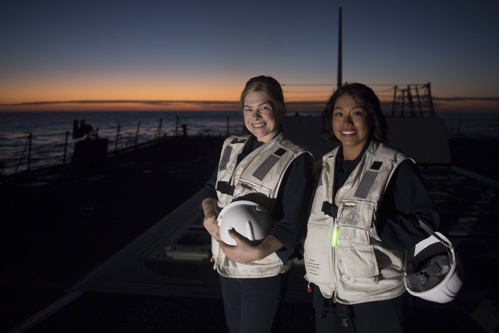 Hospital Corpsman 3rd Class Dana Horn left, and Seaman Ofelia Velasquez pose for a photo at sunset while preparing for a replenishment-at-sea aboard USS Spruance (DDG 111).