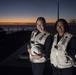 Hospital Corpsman 3rd Class Dana Horn left, and Seaman Ofelia Velasquez pose for a photo at sunset while preparing for a replenishment-at-sea aboard USS Spruance (DDG 111).