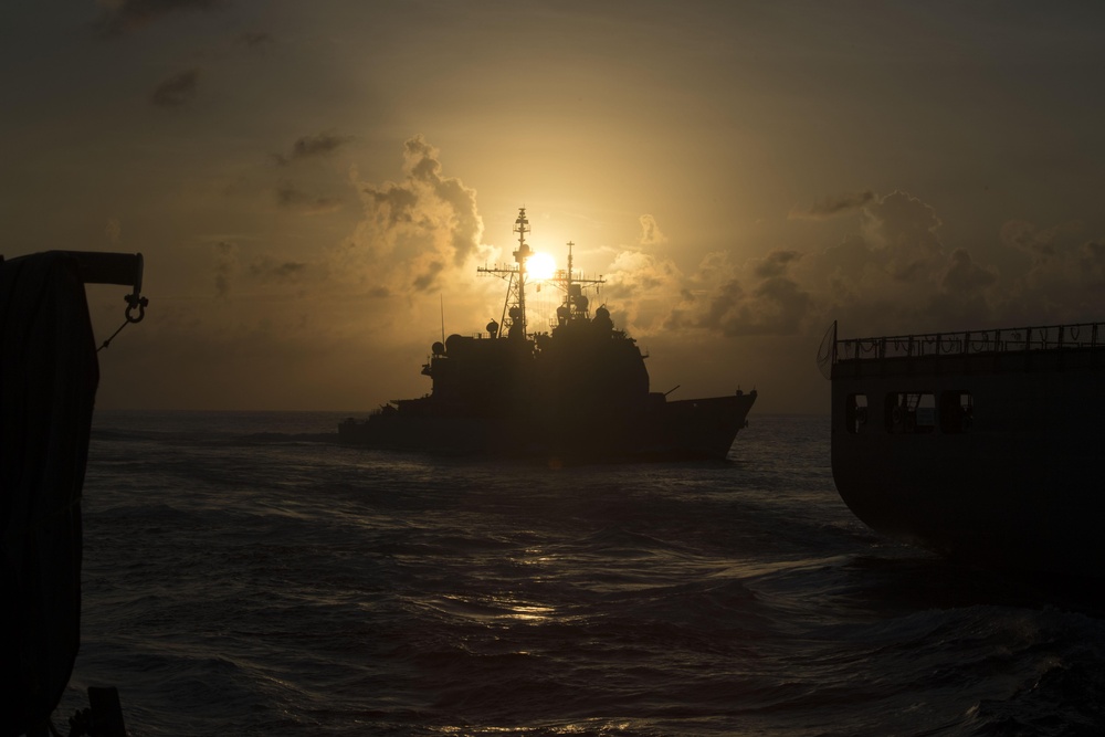 USS Mobile Bay (CG 53), center, cuts through the Pacific Ocean while pulling alongside USNS Charles Drew (T-AKE 10), right, and Spruance (DDG 111) for a replenishment-at-sea.