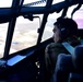 Airmen are standing on a latter looking inside an engine of a C-130J with other C-130s behind them.