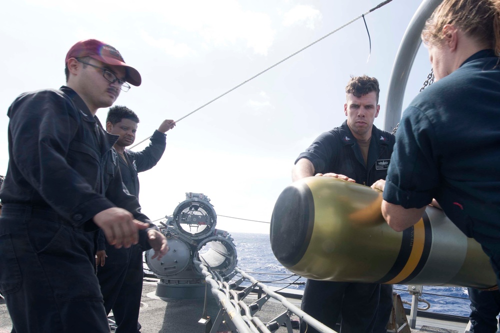 Sailors maneuver a MK 46 Mod 5A(S) torpedo while loading the launch system during maintenance aboard USS Spruance (DDG 111).