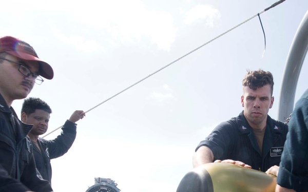 Sailors maneuver a MK 46 Mod 5A(S) torpedo while loading the launch system during maintenance aboard USS Spruance (DDG 111).