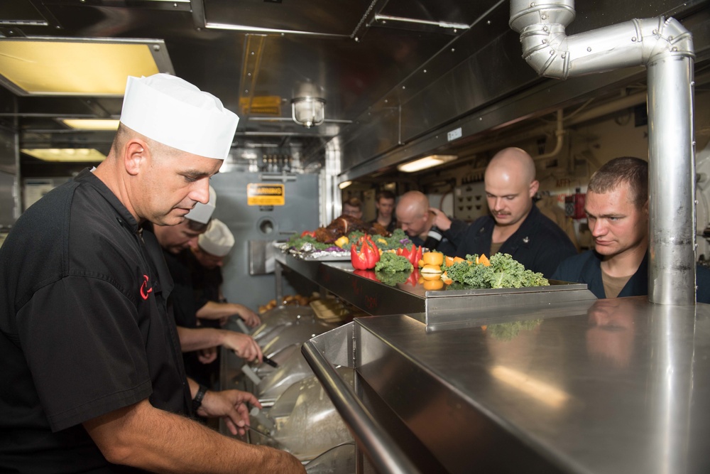 Command Master Chief Chad Schultz, left, the command master chief of USS Chung-Hoon (DDG 93), serves food to Sailors in the galley for Thanksgiving dinner.