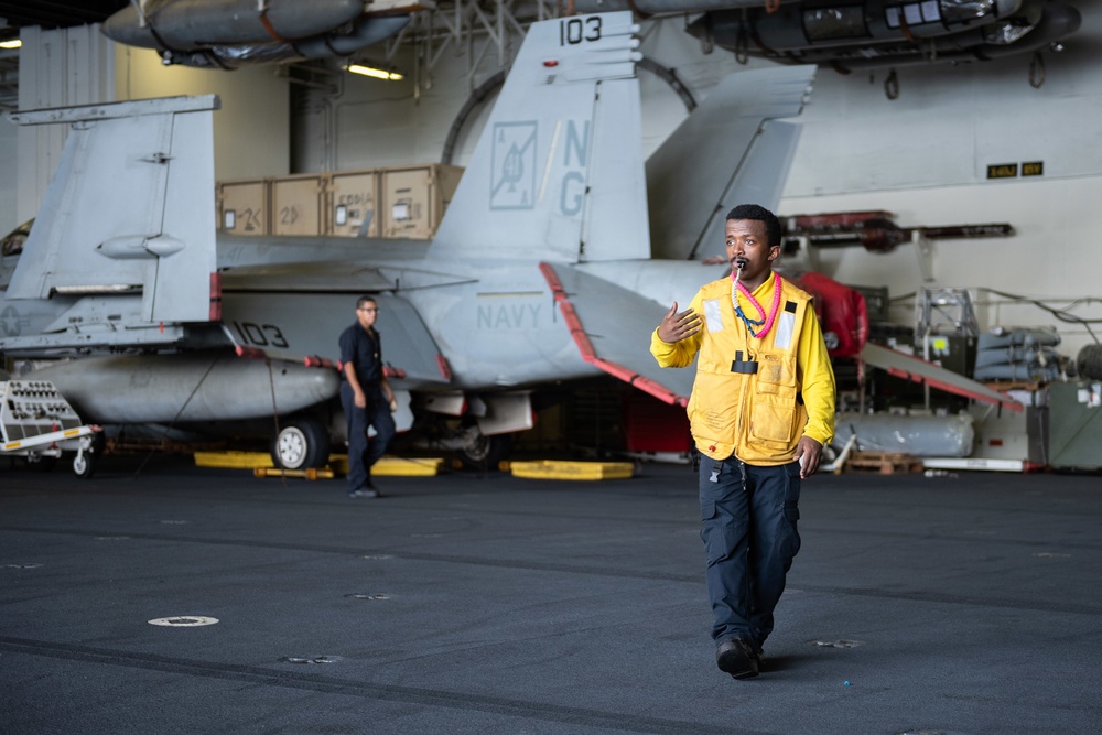 Aviation Boatswains Mate (Handling) 3rd Class Nahom Abebe, from Denver, directs an MH-60S Knight Hawk, with Helicopter Sea Combat Squadron (HSC) 14, into the hangar bay aboard the Nimitz-class aircraft carrier USS John C. Stennis (CVN 74).