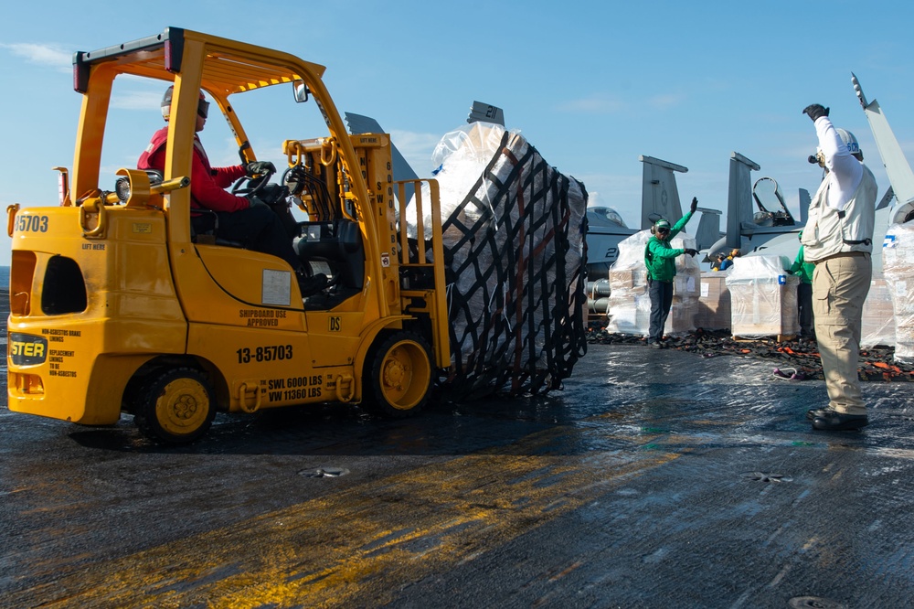 Sailors direct a forklift with pallets of cargo from the dry cargo and ammunition ship USNS Cesar Chavez (T-AKE 14) on the flight deck aboard the Nimitz-class aircraft carrier USS John C. Stennis (CVN 74) during a replenishment-at-sea.