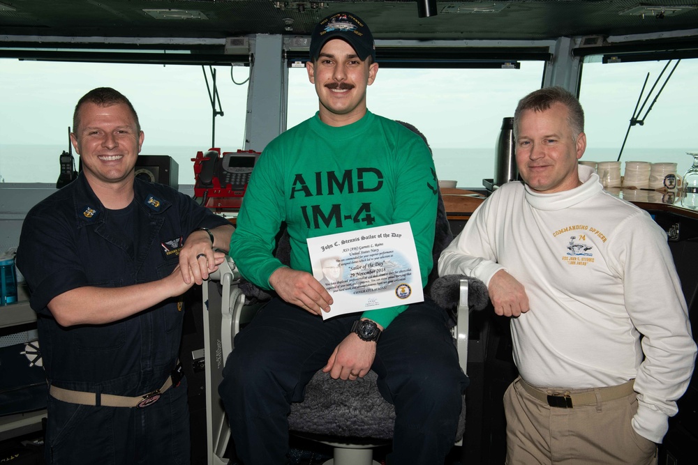 Aviation Support Equipment Technician 3rd Class Garrett Rains, center, poses for a photograph as the Sailor of the Day with Capt. Randy Peck, right, commanding officer of USS John C. Stennis (CVN 74), and Command Master Chief Benjamin Rushing.