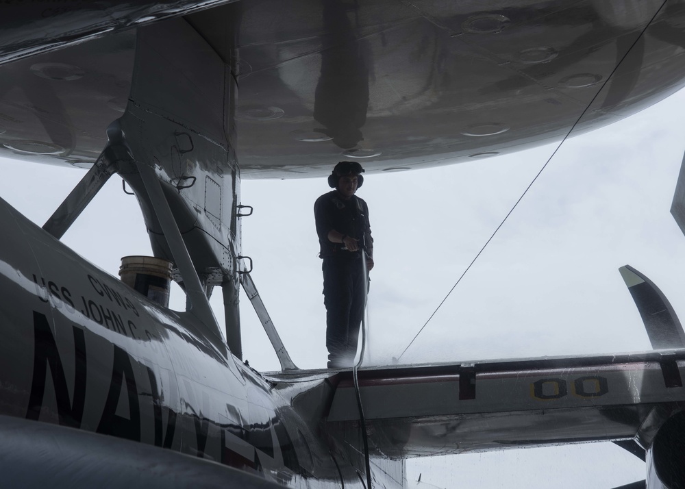 A Sailor washes an E-2C Hawkeye, with Carrier Airborne Early Warning Squadron (VAW) 117, on the flight deck aboard USS John C. Stennis (CVN 74).
