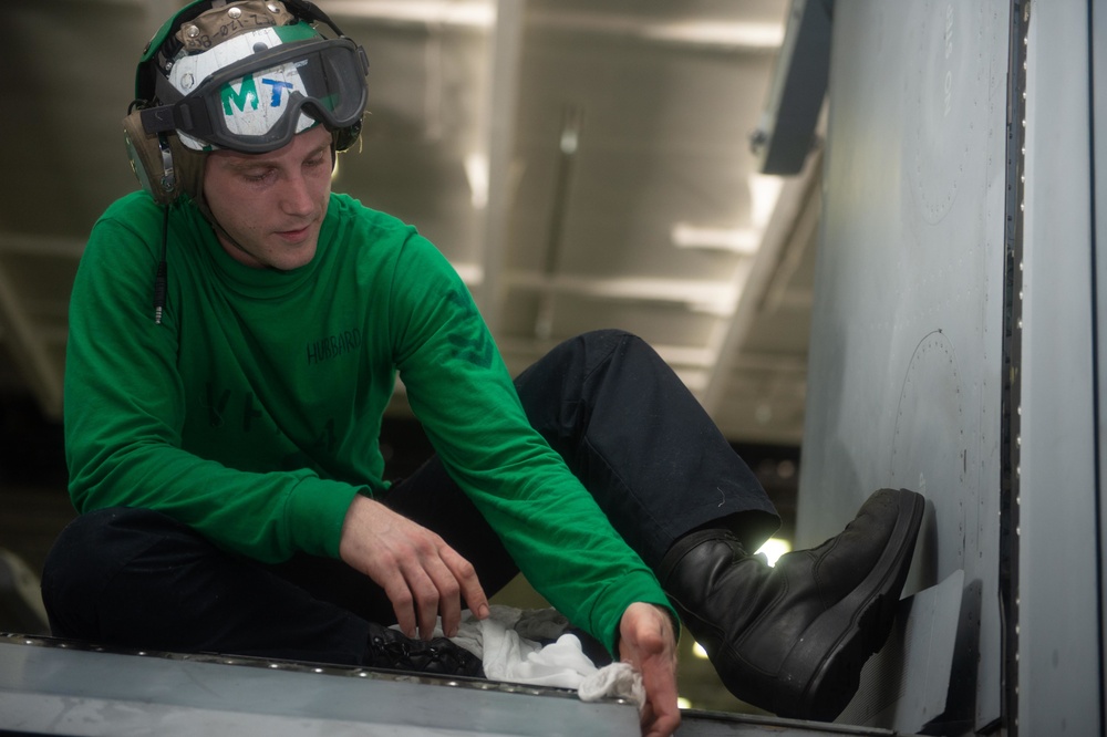 Aviation Structural Mechanic 2nd Class Kade Hubbard inspects and cleans an F/A-18F Super Hornet, with Strike Fighter Squadron (VFA) 41, in the hangar bay aboard USS John C. Stennis (CVN 74).