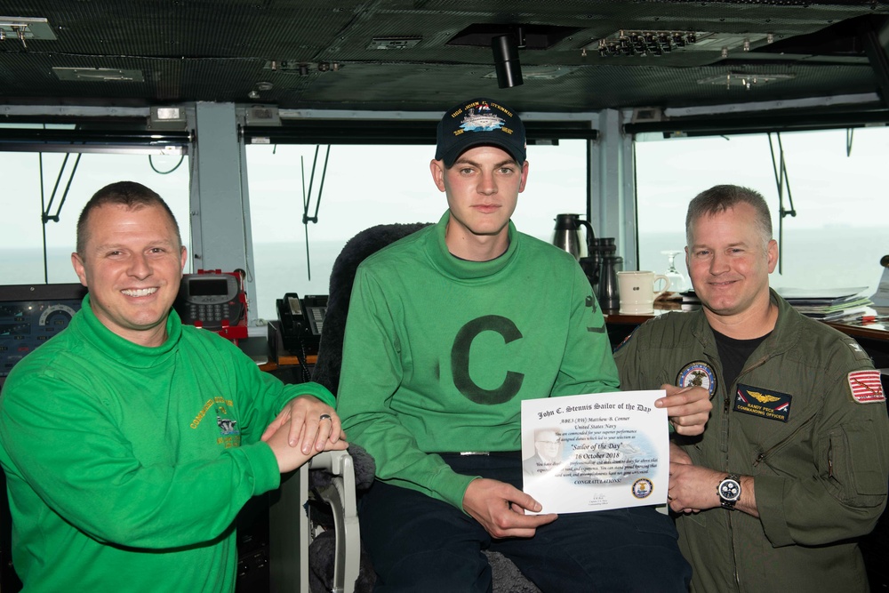 Aviation Boatswain’s Mate (Equipment) 3rd Class Matthew Conner poses for a photograph as the Sailor of the Day with Commanding Officer Capt. Randy Peck and Command Master Chief Benjamin Rushing aboard USS John C. Stennis (CVN 74).