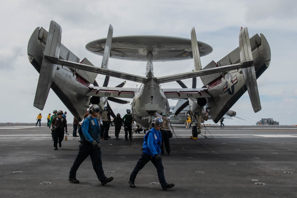 Sailors transit the flight deck behind an E-2C Hawkeye, with Carrier Airborne Early Warning Squadron (VAW) 117, aboard the Nimitz-class aircraft carrier USS John C. Stennis (CVN 74).