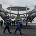 Sailors transit the flight deck behind an E-2C Hawkeye, with Carrier Airborne Early Warning Squadron (VAW) 117, aboard the Nimitz-class aircraft carrier USS John C. Stennis (CVN 74).