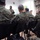 Maryland Guard, Bosnia-Herzegovina armed forces celebrate 15-year partnership A military briefing or training session is taking place indoors, with one standing presenter addressing a group of seated personnel. The presenter appears to be a female soldier in camouflage uniform speaking to an audience of approximately five or more military personnel seated in black chairs. The setting includes a whiteboard, a flag on the wall, and camouflage-patterned curtains or fabric.