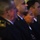 Maryland Guard, Bosnia-Herzegovina armed forces celebrate 15-year partnership The image shows a group of individuals in dark military or law enforcement dress uniforms attending what appears to be a formal ceremony or event. The subjects are seated in a row, facing the same direction, suggesting they are watching a presentation or program. The lighting is dramatic and low, creating a moody, formal atmosphere.