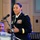 Maryland Guard, Bosnia-Herzegovina armed forces celebrate 15-year partnership A female U.S. Army officer in dress blues is delivering a speech at a podium with a microphone. She is wearing multiple service ribbons and medals, and gold shoulder boards indicating senior officer rank. A second individual, partially visible in the background, is seated behind her.