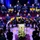 Maryland Guard, Bosnia-Herzegovina armed forces celebrate 15-year partnership A formal military ceremony or concert is taking place in an auditorium, featuring a large military band seated on a raised stage. A person in a dark military uniform is speaking at a podium bearing what appears to be a Bosnian Armed Forces emblem. An audience of civilians and military personnel is seated in the foreground.