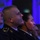 Maryland Guard, Bosnia-Herzegovina armed forces celebrate 15-year partnership Three individuals in military or law enforcement dress uniforms are seated in an audience, appearing to watch a presentation or ceremony. The scene is illuminated by blue ambient lighting, suggesting a formal indoor event. The subjects are captured in profile or three-quarter view, with the foreground and background figures slightly out of focus.