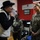 Maryland Guard, Bosnia-Herzegovina armed forces celebrate 15-year partnership Three individuals are engaged in conversation inside an 'American Corners' facility located in Zenica. Two women in military camouflage uniforms (one US Army, one US Air Force) are speaking with a civilian man wearing a black wide-brimmed hat and a beige vest. The atmosphere appears friendly and informal, with all three smiling.