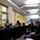 Maryland Guard, Bosnia-Herzegovina armed forces celebrate 15-year partnership Two U.S. Army soldiers in camouflage uniforms are seated at a dark conference table, with one appearing to address a group of civilians seated in a semi-circle. The setting appears to be an official meeting room or community center, with yellow vertical blinds, framed photos on the wall, and indoor plants. A person in the foreground wearing a jacket with a U.S. flag patch is also present, suggesting a community engagement or outreach event.