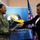 Maryland Guard, Bosnia-Herzegovina armed forces celebrate 15-year partnership A U.S. Army soldier in multicam uniform is exchanging or receiving a plaque/award with a civilian woman in front of a Bosnia and Herzegovina Ministry of Defence backdrop. The setting appears to be an official bilateral military or diplomatic ceremony. Both individuals are smiling and engaged in a formal presentation gesture.