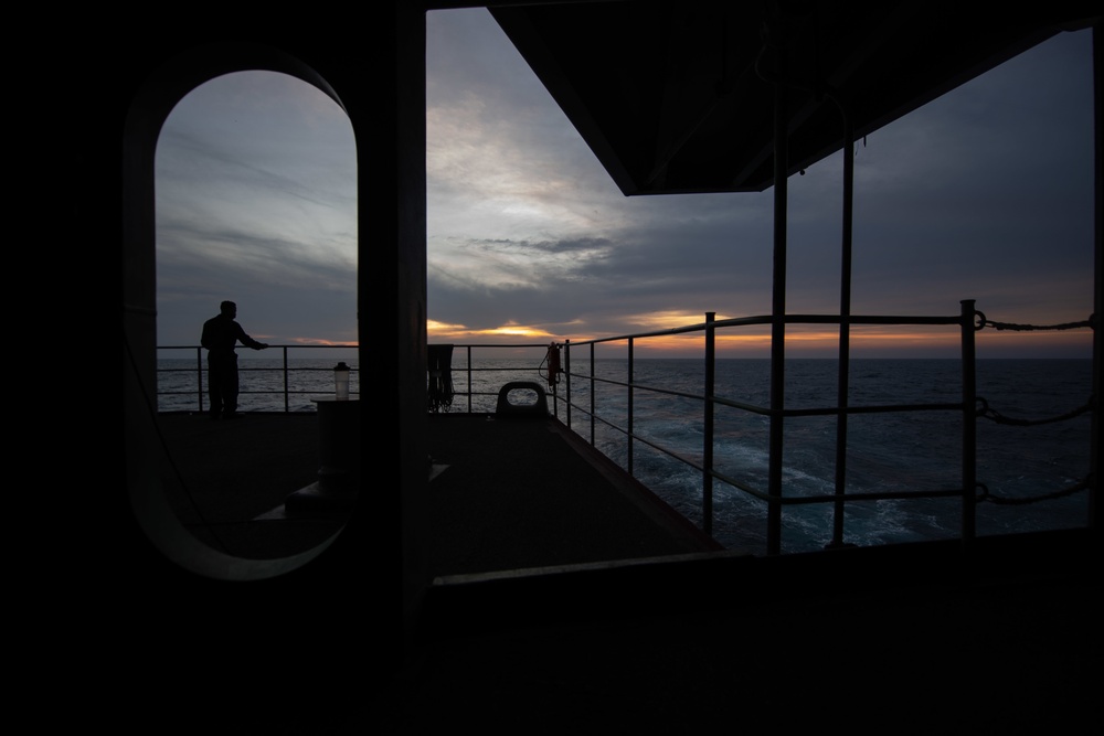 A Sailor watches the sunset from the fantail aboard the Nimitz-class aircraft carrier USS John C. Stennis (CVN 74).