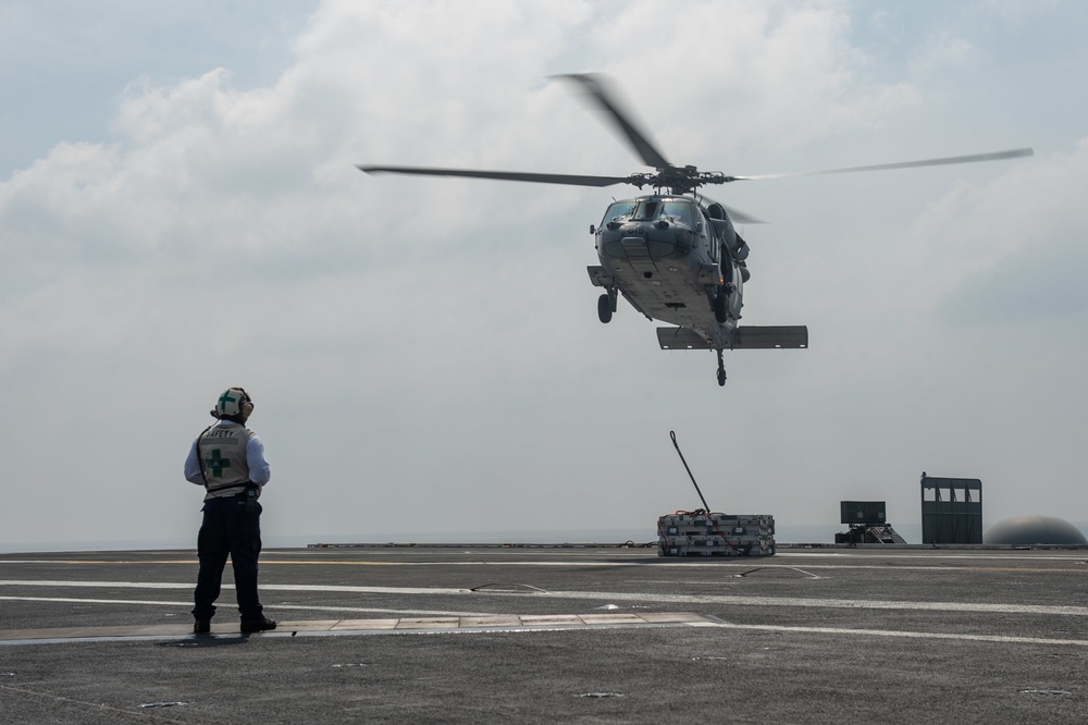 A Sailor observes an MH-60S Knight Hawk, with Helicopter Sea Combat Squadron (HSC) 14, deliver ammunition to the flight deck during a vertical replenishment aboard the Nimitz-class aircraft carrier USS John C. Stennis (CVN 74).