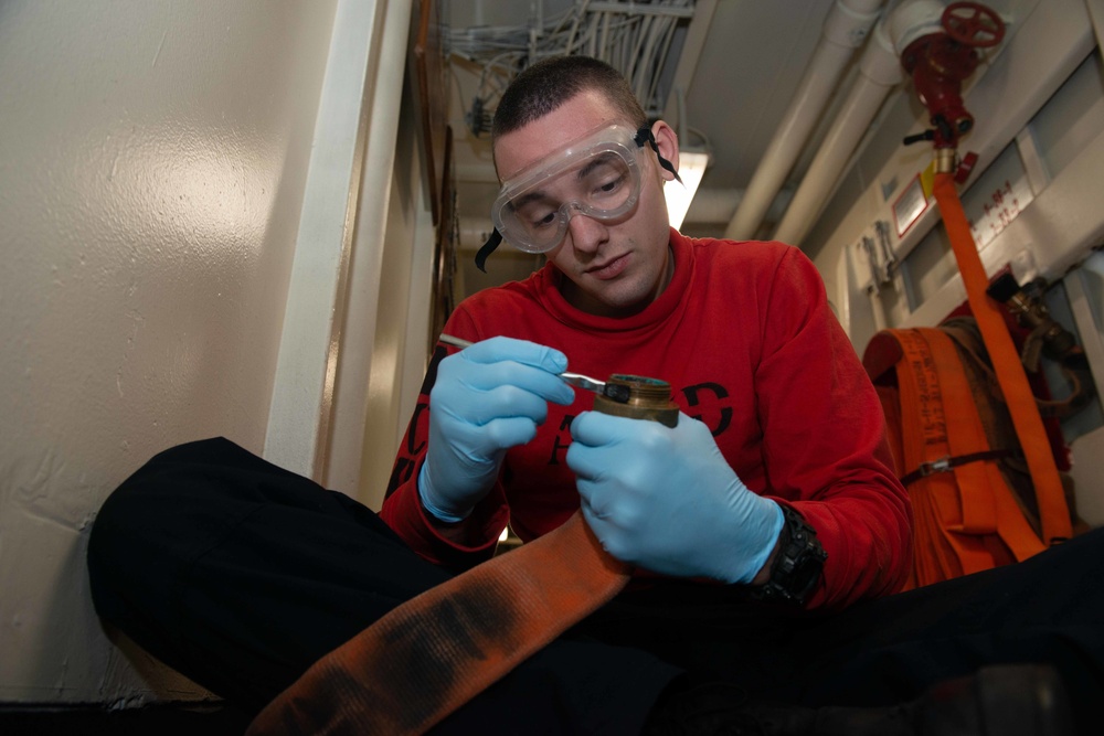 U.S. Navy Sailor conducts maintenance on a fire hose