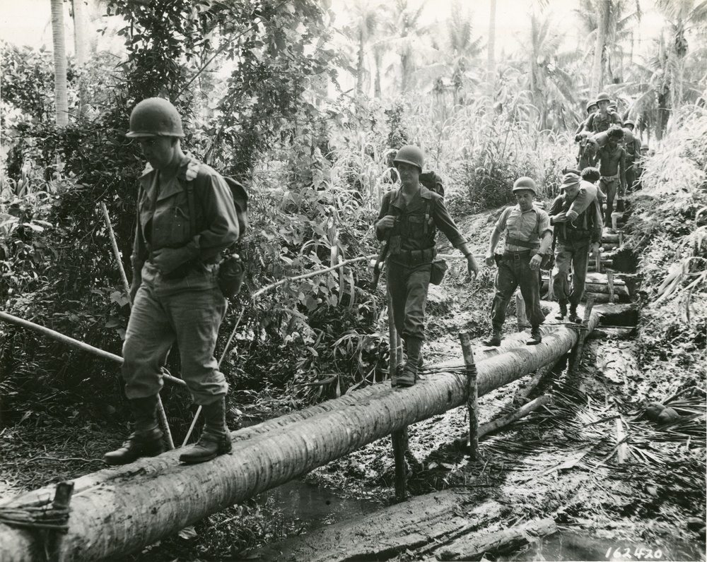 32nd Division Soldiers cross a rudimentary log bridge in the South Pacific in 1942 during World War II