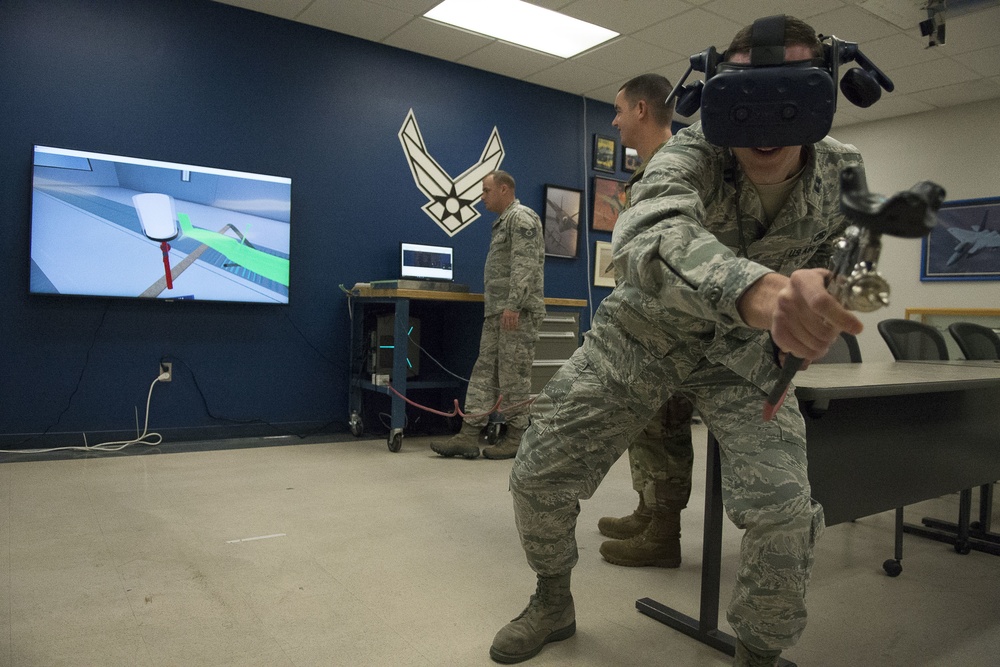 Capt. Patrick Britton, 359 Training Squadron Detachment 1 commander, right, uses a spray gun and HTC Virtual Reality goggles to apply paint to a virtual aircraft part in a 3-D VR trainer