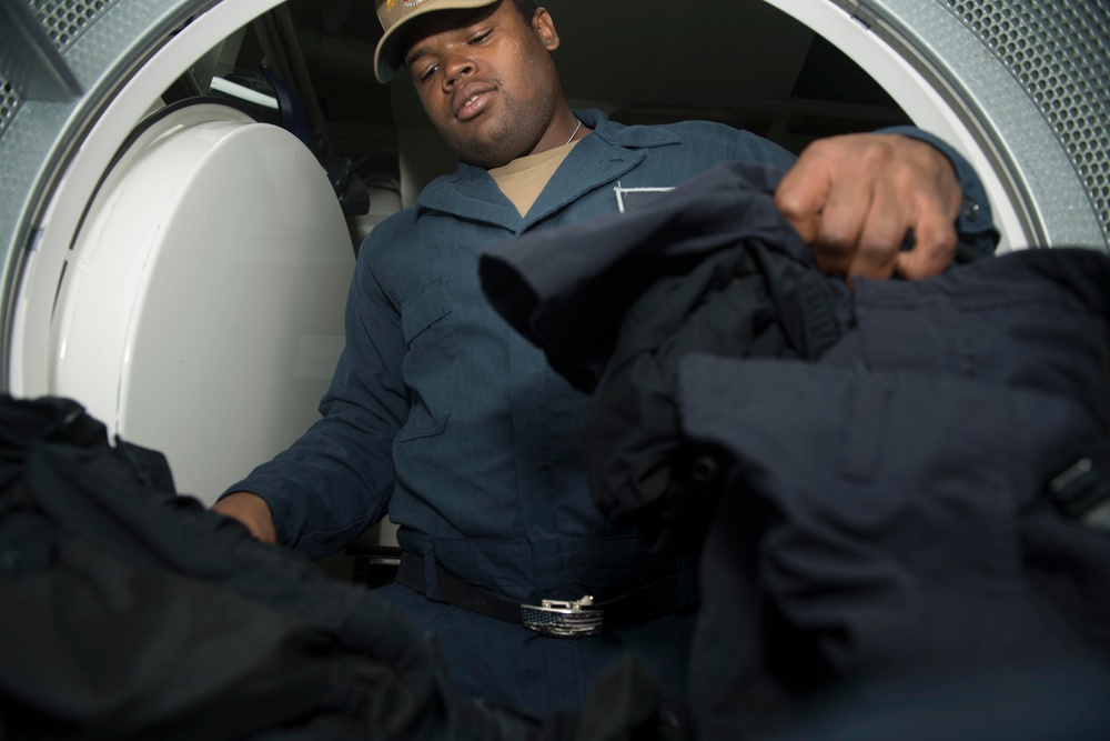U.S. Navy Ship's Serviceman Seaman Trevor Player, from Shreveport, Louisiana, places uniforms in a dryer