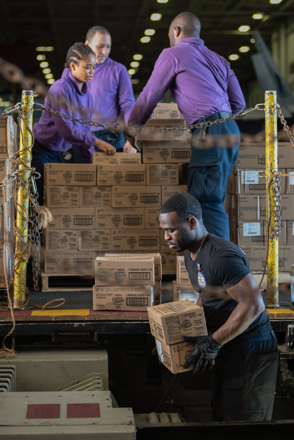 U.S. Sailors load boxes onto a conveyor aboard USS John C. Stennis