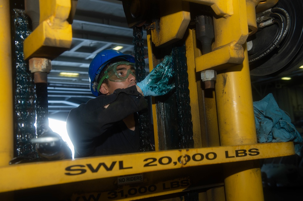 U.S. Sailor greases a lift chain on a forklift