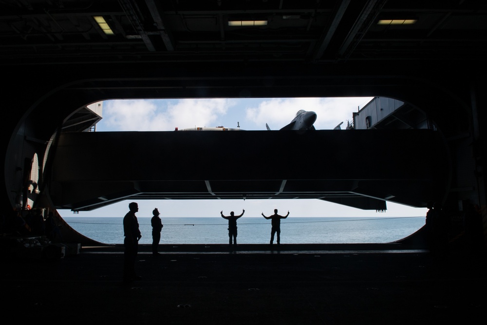 U.S. Sailors signal to raise an aircraft elevator