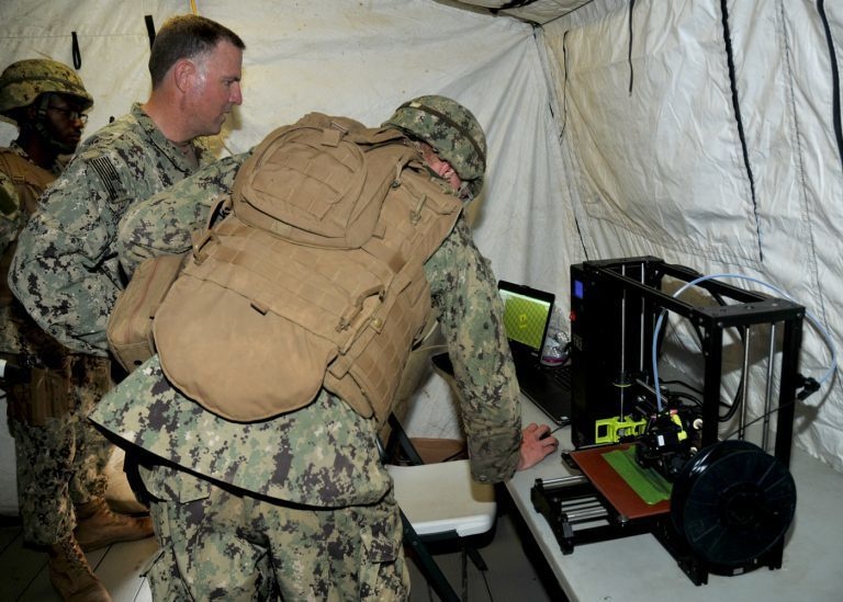 Rear Adm. Brian Brakke, Commander, Navy Expeditionary Combat Command, is briefed on the capabilities of additive manufacturing using a 3-D printer.