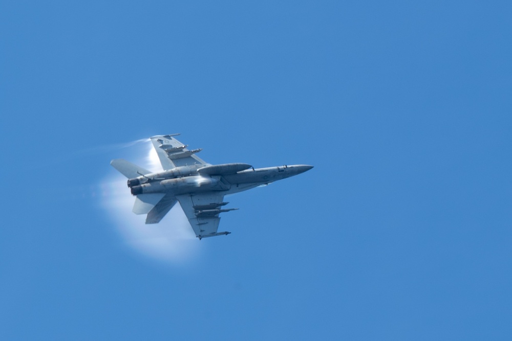 An F/A-18E Super Hornet flies over the aircraft carrier USS John C. Stennis (CVN 74)