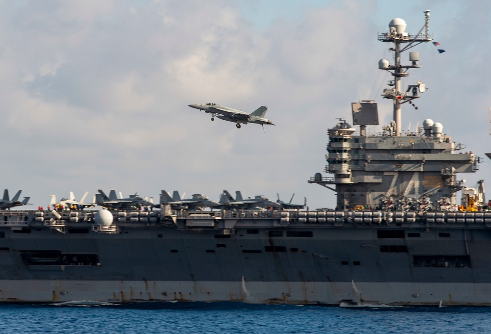 An F/A-18E Super Hornet flies over the flight deck of the aircraft carrier USS John C. Stennis (CVN 74)