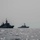 Two naval warships are operating in open sea under overcast, hazy conditions. The foreground vessel bears the hull number F946, identifiable as a frigate-class warship, while a second larger warship — appearing to be an Arleigh Burke-class destroyer — is visible in the background to the right. The image appears to document a joint naval exercise or patrol operation.