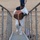 A person wearing a white protective/Tyvek suit and a USS McNulty DDG cap is carrying a coiled fire hose up a metal gangway or staircase. They are wearing black gloves and safety glasses, suggesting a work or cleanup operation. A second person in dark clothing is visible in the background on a sandy surface.