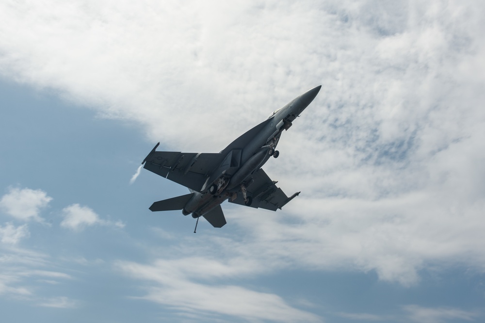 An F/A-18E Super Hornet flies over the flight deck of the aircraft carrier USS John C. Stennis (CVN 74)