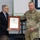 A U.S. Army soldier in OCP (Operational Camouflage Pattern) uniform is presenting or receiving a framed certificate from a civilian man in a dark suit. The framed document appears to be a State of Texas Citation. The ceremony appears to be taking place in an indoor setting, likely a classroom or meeting room.