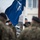 20th anniversary of NATO expansion Military personnel in camouflage uniforms are raising or holding a NATO flag during what appears to be a formal ceremony. The soldiers are wearing various colored berets, suggesting a multinational or multi-branch military gathering. The setting appears to be a military installation in cold, overcast weather conditions.