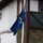 20th anniversary of NATO expansion Three military personnel in camouflage uniforms and blue berets are raising a NATO flag during a formal ceremony. One soldier on the left is saluting while two others handle the flagpole. A partial Swedish flag is visible on the right edge of the frame, suggesting a multinational military context.