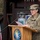 20th anniversary of NATO expansion A U.S. Army Brigadier General (one star rank visible on cap) is speaking at a podium during an official ceremony. The podium bears the emblem of the Polish Military Contingent, and a Polish flag is visible to the left. The setting appears to be an outdoor or semi-outdoor military installation in Poland.
