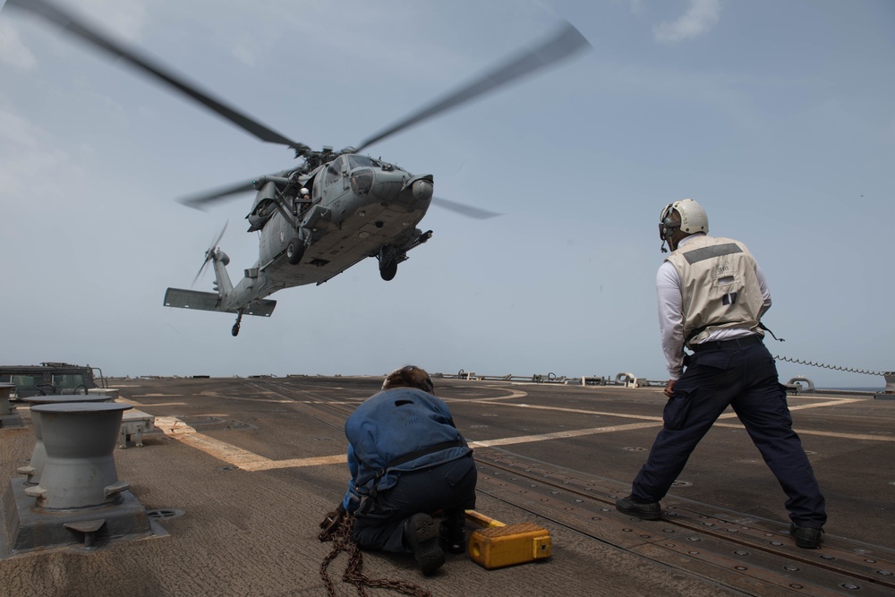 U.S. Navy Ship’s Serviceman and U.S. Navy Boatswain’s Mate, brace as an MH-60S Sea Hawk prepares to land