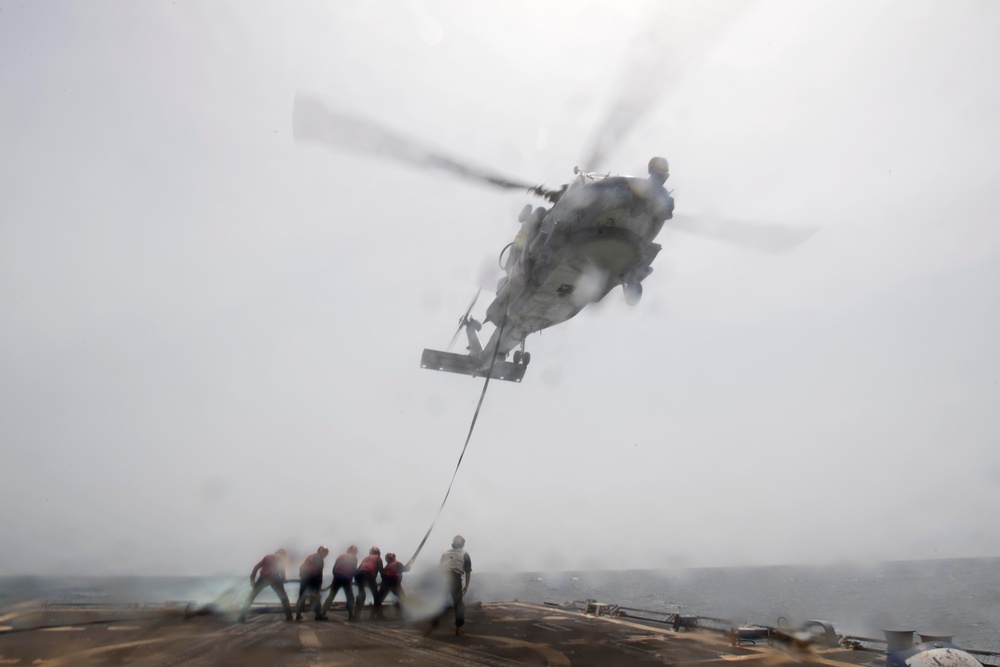 U.S. Sailors perform an inflight refueling with an MH-60R Sea Hawk on the flight deck of USS Spruance