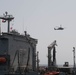 An MH-60R Sea Hawk flies near the fleet replenishment oiler USNS Kanawha