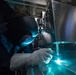 U.S. Navy Hull Maintenance Technician welds a coffee machine to a table aboard USS Stockdale